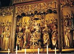 The central section of an elaborately carved, painted and gilded altarpiece showing the Virgin Mary and Christ Child seated in majesty and surrounded by saints and angels. Although the flesh and some details are painted in colour, most of the surfaces are gilt. The figures are all chubby-faced and have a charming quality.