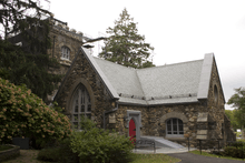 An L-shaped stone building with a pointed roof and a red door at the right end, similar to the tower shown above, which is visible in the left rear