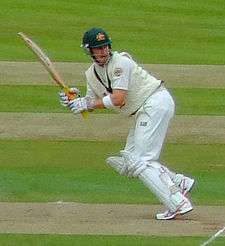 A man in cricket whites and baggy green walking towards the camera