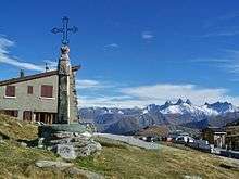 A view from the summit of a mountain with a cross monument on the left.