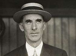 Head shot of Caucasian man wearing a hat. The top of his dark jacket and tie are visible.