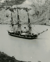 Photograph of a ship being towed through a canal