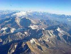 A view downward of rocky, jagged mountains with some snow cover