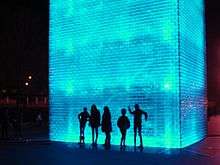 Tourists silhouette themselves against the fountain's lighting at night.