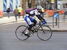 A man with sports clothes and a white helmet on a bicycle on a road.