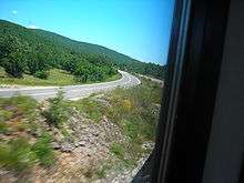 A view of a road from a side, showing two traffic lanes of a single carriageway as the road follows a left curve