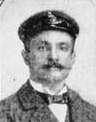 Head of a white man with handlebar mustache wearing a suit and bow tie and peaked cap.