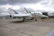 Side view of white jet aircraft parked with other aircraft in the background