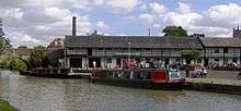 Water with two narrow boats and bridge. On the far side is a white coloured building displaying a banner which says Canal Museum and Shop.