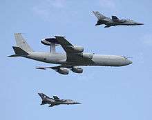 Four-engined jet aircraft with disc-shaped radar on fuselage in-flight flanked by two jet fighters.