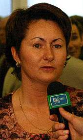 A woman with brown hair, speaking into a microphone.