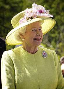 Elderly lady with a yellow hat and grey hair is smiling in outdoor setting.