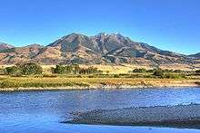 A river flows through a flat valley with mountains in the background.