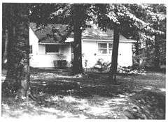 alt=Small cottage partially hidden by large trees