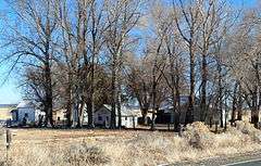 Photograph of the Eskelin Ranch, including a house and several agricultural buildings shaded by tall trees on a broad treeless plain