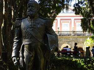 A bronze statue of a bearded man in military uniform stands among trees in a park