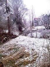 Late snow covers a meadow and brook bank.