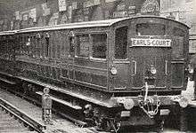 A three-quarter black-and-white photograph of a train standing at a station, showing the end carriage with windows at the end