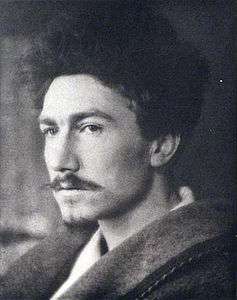 Black-and-white photograph of a dark-haired man with a moustache and goatee, peering leftward