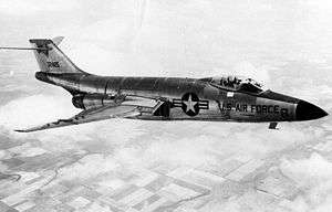 Black-and-white photo of jet aircraft flying right above clouds. On the aircraft's side is a symbol with a star, to the right of which says U.S. Air Force. Its horizontal stabilizers are located atop its fin.