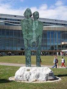 A photograph of a large, stylized, verdigreen, icon-like statue depicting, in outline, two parents and a child