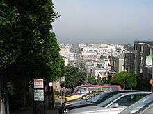 City landscape, with gray skies above the windshields of parked cars overlooking the distinctive buildings of San Francisco.