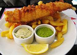 Fried fish on a pile of fried potato, with ramekins of tartar sauce and mushy peas.