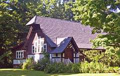 A brown and white building with high, steep roof hanging over at one end in the middle of some trees