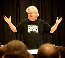 Photo of a man in giving a presentation to an audience in front of a theatrical curtain