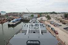 Looking down the front of a ship towards the yard, with artillery guns in the foreground and the buildings of the yard in the background