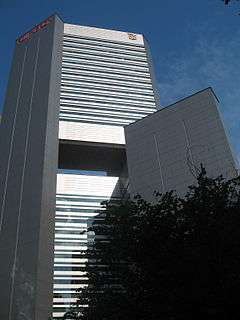 Box-like structure with grey, windowless siding and a large hole near the centre of the tower