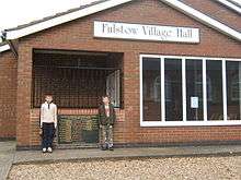 Frontage of a brick-built hall with two young children standing by the entrance.