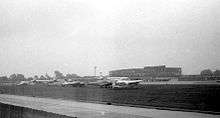 Small planes parked next to a runway, with terminal building in background