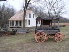 Wooden cart with orange wheels in a field, in front of a white house