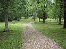 A gravel path runs across grass dotted with trees