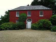 Red two-story house amid trees and bushes.