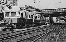 Black and white photograph of the bridge, with train and tracks in the foreground