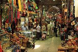 Goods overflow out of storefronts, leaving a narrow passageway where shoppers move about.