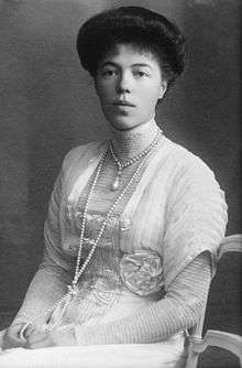 Black-and-white photograph of a young Olga seated in an Edwardian dress with a high neck line and long sleeves. Her thick dark hair is pinned up, and she wears a rope of pearls around her neck.