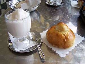 A frozen white dessert in a clear glass, next to a piece of bread