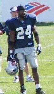 Color photograph of African-American football player Guss Scott in the dark blue, white and red uniform of the New England Patriots, standing on the sidelines at training camp.