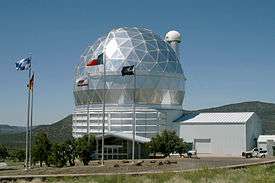 A silver geodesic dome against a blue sky, with flags in the foreground.