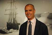 Worsley smiling in front of a montage of battleships