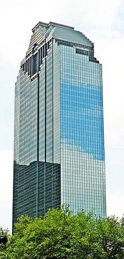 Tall, glass-block tower with subtle setbacks and granite Mayan flat-topped pyramid at the top. Directly under this is a granite reverse pyramid shape with rows of vertical bars with glass insets.