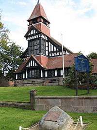 A church seen from the west showing timber framing, brickwork, windows, and a tower with a lead spire