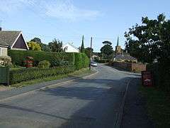 Semi-suburban village road, with the copper-clad church spire in the distance.