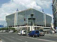 On the other side of a busy intersection, sits a low-rise, glass-faced building.  Two large Hilton logos are mounted on the edge of the roof, and a line of flagpoles are outside the building.