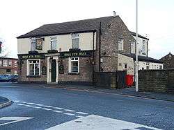 A brick-built public house on a street corner, with its name displayed along the front of the building