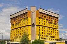 A 12-story hotel building with a yellow- and brown-coloured exterior.  Trees are visible in the foreground, and the building reads "Holiday Inn" at the top.