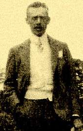 Photo of Burnham's brother Mather Howard Burnham.  Howard is wearing a suit and tie and standing with his right hand in his pocket.